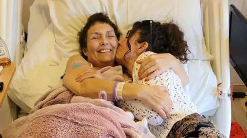 Handout Kayleigh Jones lying down on a hospital bed hugging and kissing her mum