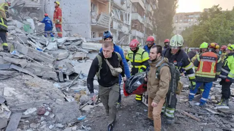 Rescuers at the site of damanged residential buildings with rubble in the background on a sunny day in Kyiv