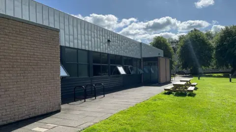 A brick leisure building with windows and grass and benches outside