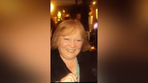 Family handout A smiling woman in a pub or restaurant setting. She is wearing a black cardigan and a blue top  