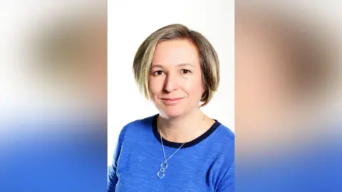 Central Bedfordshire Council Tracey Wye is wearing a blue top with a dark navy neckline and a silver necklace with two interlinked circles. Her hair is short, layered and highlighted. The background is plain white.