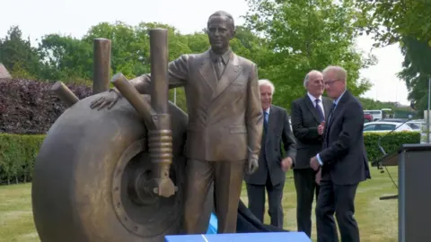 Statue of man being unveiled by gentlemen in black suits.
