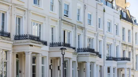 A stock image of a row of white houses with porticos at each entrance and small black railings above each one.