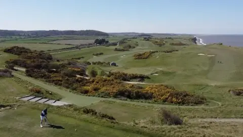 Jamie Niblock/BBC An aerial image of a golfer playing on a golf course next to the sea.