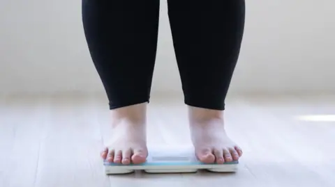 An anonymous woman who is overweight stands on some weighing scales