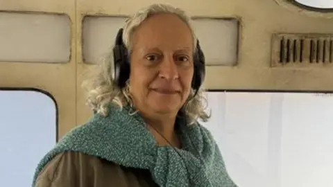 Khadijah Hasan A lady wearing headphones and smiling at the camera.