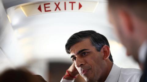 Rishi Sunak underneath an "exit" sign on the campaign plane