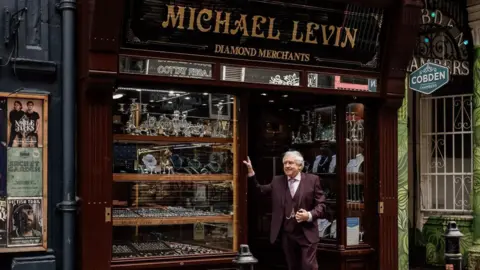 Michael Levin Jewellers Grenville Price, in a suit, stands outside his shop, which has a traditional wood and glass frontage