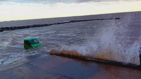 A green flatbed truck can be seen in the waves on Cleethorpes beach at high tide. 