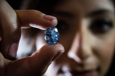 A model poses with the De Beers Millennium Jewel 4, a rare Oval Internally Flawless Fancy Vivid Blue Diamond weighing 10.10 carats the largest oval fancy vivid blue diamond ever to appear at auction, which is expected to reach between £21,200,000 - £24,700,000 GBP (27,000,000 - 31,600,000 Euros, $ 30 - 35m USD), at a press preview in London on March 15, 2016. 