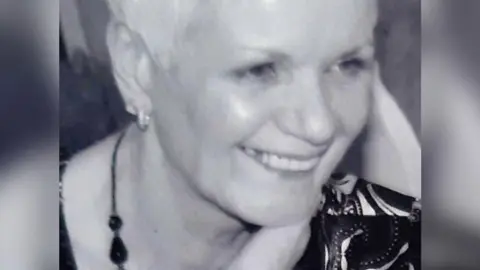 Police Scotland A black and white shot of Judith Molloy smiling and looking to the side of the camera. She has short light hair and is wearing a dark necklace and a patterned top.