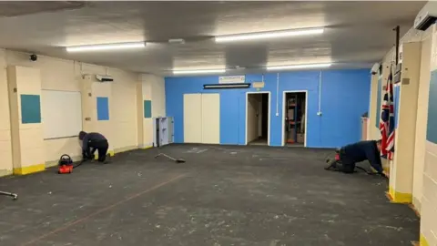 Efficiency North A scout hut with painted bricks in white, yellow and blue. Two men crouch in the corners cleaning.