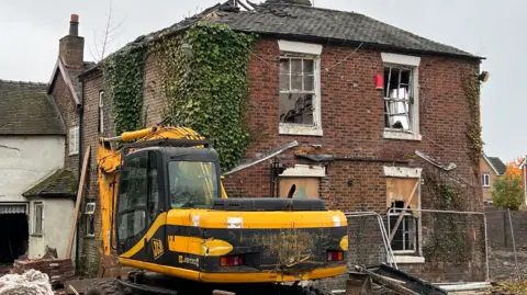 LDRS A mechanical digger outside a wreck of a house