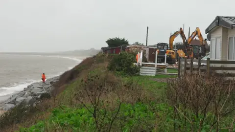 Stephen Huntley/BBC Chalets being demolished by diggers
