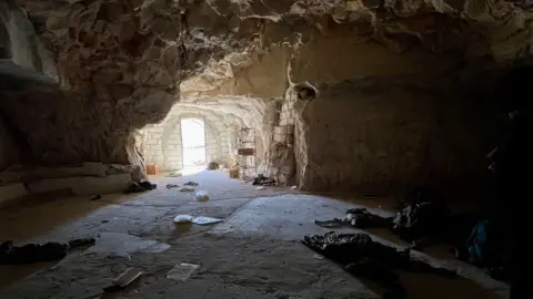 A cave. The image is shot from the inside, with light streaming in through the opening to the cave on the far side