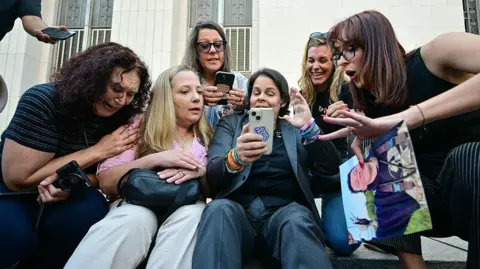 Getty Images A group of women sit on steps in front of an Los Angeles courthouse and react with happiness and tears at verdict 
