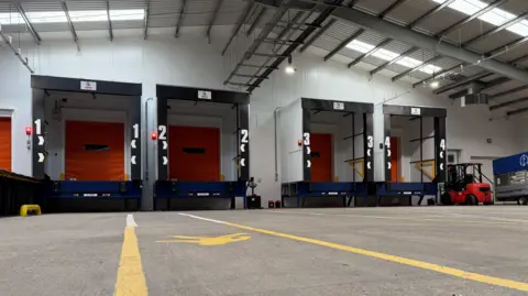 An empty indoor site for loading and unloading lorries. It looks industrial with white light and heavy equipment in view. 