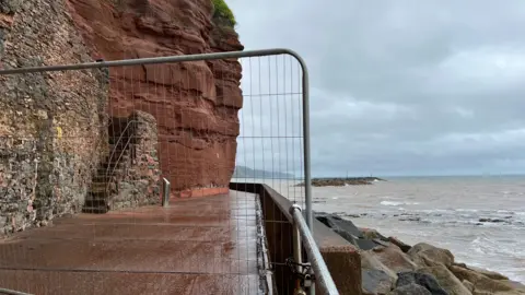 The Millenium Walkway in Sidmouth with a fence in front of the entrance and the sea on the right