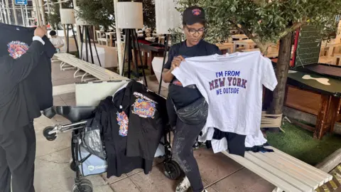 Grace Eliza Goodwin/BBC a woman holds up Knicks tshirts