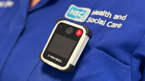 A small camera device attached to the front of a blue nurses uniform. 