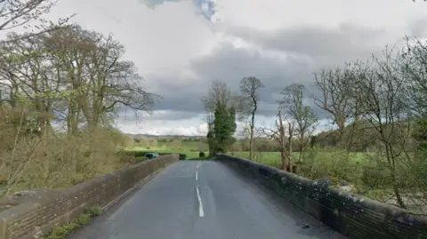 A two-lane bridge runs over a river, with trees and countryside all around.