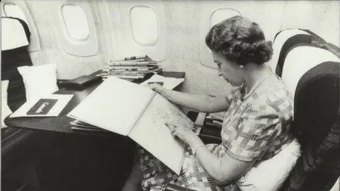 British Airways Photograph of Queen Elizabeth II on Concorde in 1977. The image is from British Airways and the monarch is pictured working at a table on board the aircraft.