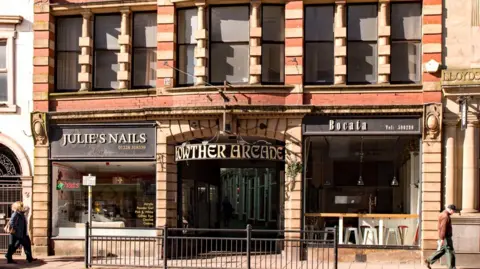 The outside of the arcade, which has a metal sign outside, a big entrance and is a red and stone brick building