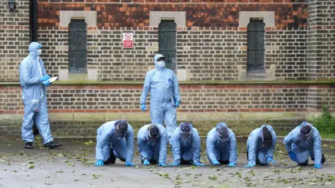 PA Media Forensic officers on all-fours carrying out search outside church in Hackney