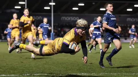 Henry Pollock flying in a dive over the tryline while holding the ball under one arm close to his chest about to score a try