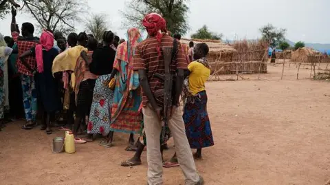 Getty Images A man with a rifle strapped to his back stands in a line with several others. 