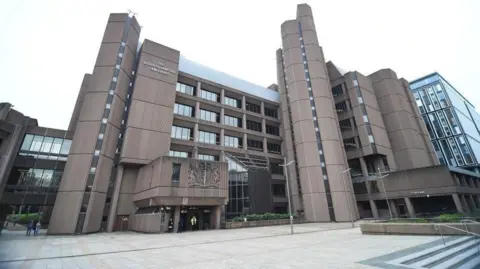 PA Media A general view of the front of Liverpool Crown Court - a multi-storey brown building. A courtyard is in front of it with steps visible on our right.