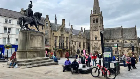 BBC A general view of the Market Place in Durham city centre. There are a few people sitting on the monument steps.