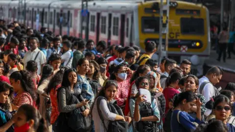 A few dozen people at a rail platform. A train is on the track