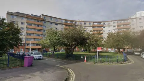 A block of curved flats which are mainly white with orange balconies.