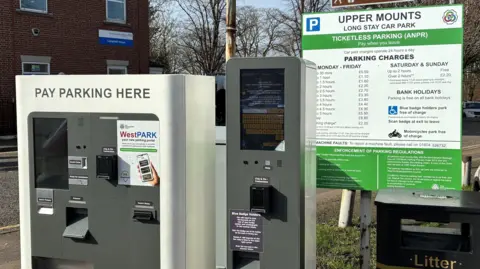 A car park machines, with a car park sign in a car park. There are two machines and one sign. 