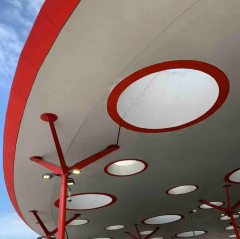 Tom Hicks The roof of Walsall bus station is a curved white structure outlined in red. It has circular holes cut into it, again outlined in red, with red metal posts. 