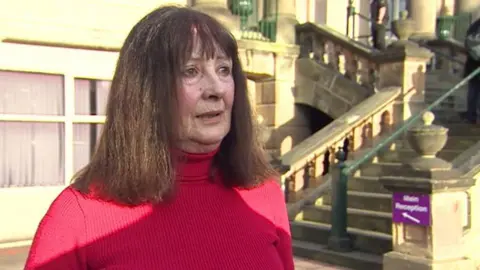 Head and shoulders shot of Angela Morgan. She has brown hair and is wearing a red jumper. 