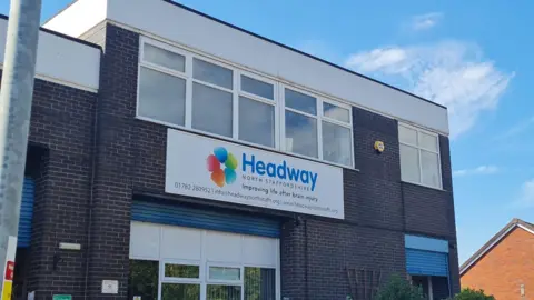 A brick-built, two-storey building, with a white sign on the front including blue lettering that readds Headway. The image is set against a blue sky with light clouds.