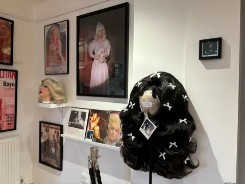 Two wigs - one with long black hair and the other with shorter blonde hair - can be seen on display at the exhibition, along with framed photographs. 