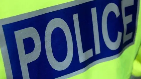 A close up of the back of a police officer's high visibility jacket. The word "police" is in silver lettering on a dark blue background.