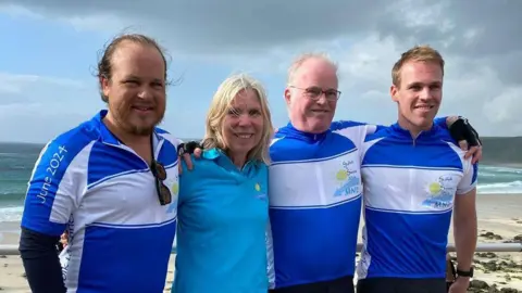 Supplied A woman wearing a blue top with three men standing either side of her. They are wearing blue and white cycling tops and are all smiling but looking away from the camera. 