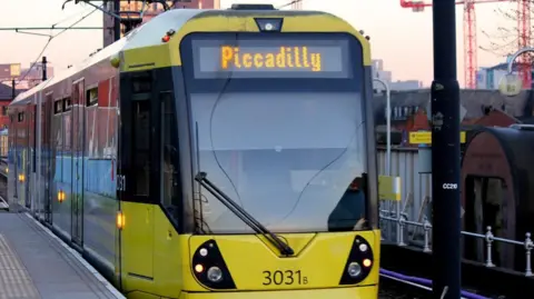 BBC Yellow Metrolink tram at a stop with Piccadilly written on the front