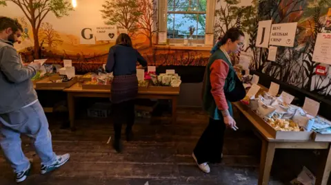 The Robin Hood Three people in a pub room looking at tables laid out with lots of different packets of crisps. Each table has a poster with a title such as "Best artisan crisp" 