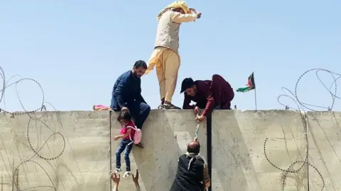 Afghans scaling a wall to access Kabul airport during the evacuation in 2021