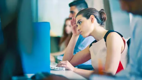 Getty Images Trabajadora de oficina sentada frente a su computadora luciendo estresada.