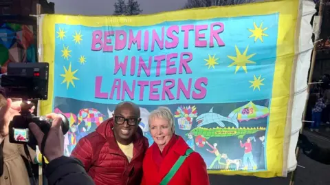 Ade Williams on the left, next to the area's MP Karin Smyth on the right, in front of an illuminated banner reading "Bedminster Winter Lanterns"