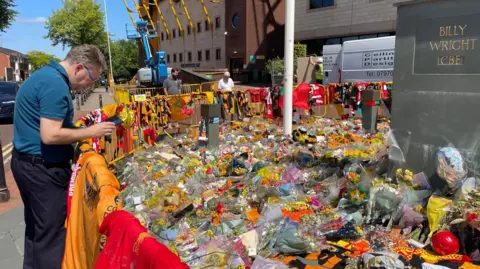 A man looks on at the many tributes laid at the ground in a circle by the Billy Wright statue.