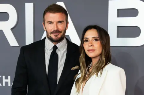 David and Victoria Beckham stand side by side and smile at the camera.