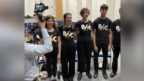 Members of the Brighton Festival Youth Choir being filmed by BBC South East at Brighton Aldridge Community Academy, Brighton. The five singers pictured were the members of the choir who all sang on the original recording of the Wander to Wonder soundtrack.