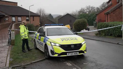 PA Media A police officer in yellow high-viz coat next to a police car